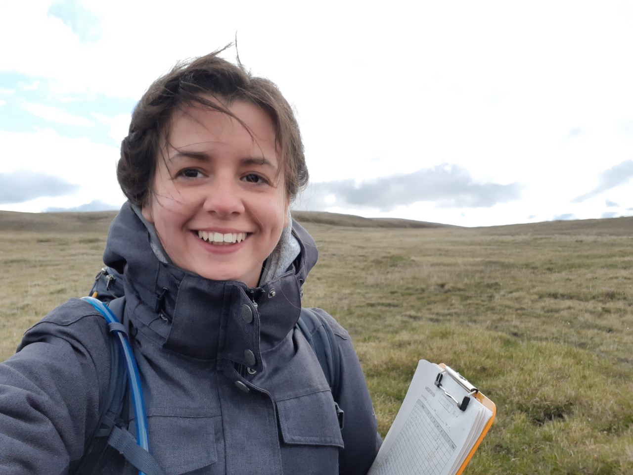 Photo headshot of smiling woman outdoors with tundra behind her.